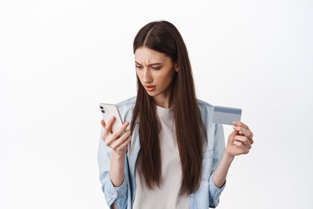 brunette-girl-looks-confused-smartphone-screen-holding-credit-card-cant-understand-how-register-card-place-order-standing-white-wall.jpg телефон